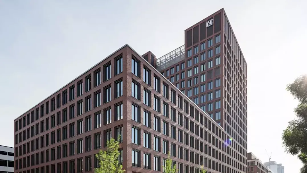 Exterior of a multi-storey red-brick office building with a ‘DB’ (Deutsche Bahn) logo on the tower against a clear sky